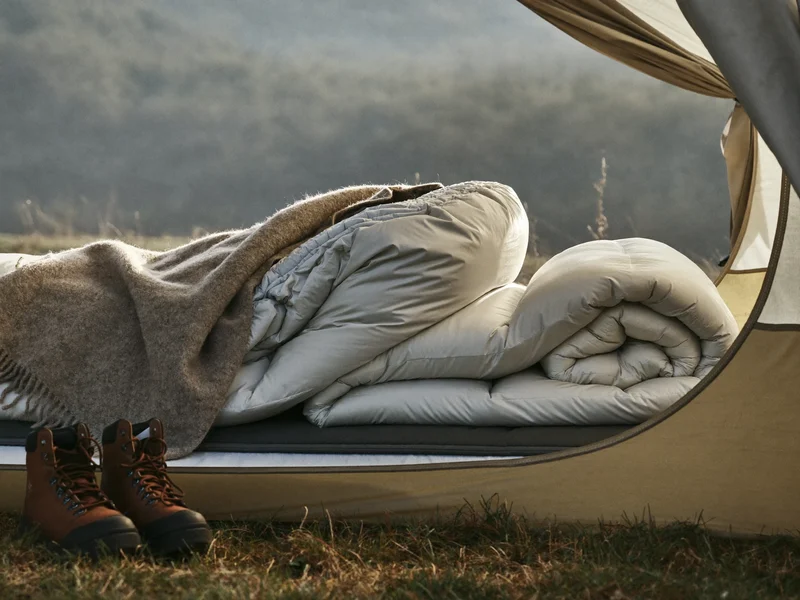Offener Zelteingang mit Daunenschlafsack, Isomatte, Wolldecke und Wanderstiefeln im Morgenlicht